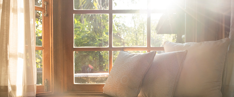 The sun shining through a window onto 3 white throw pillows.