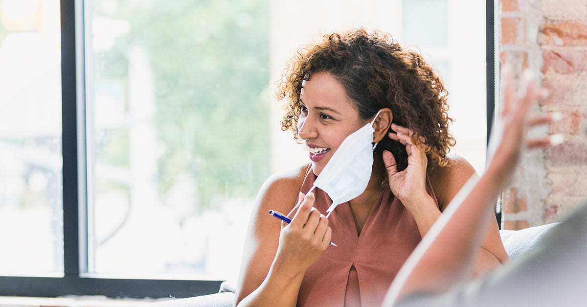A woman removing a surgical-style disposable face mask.