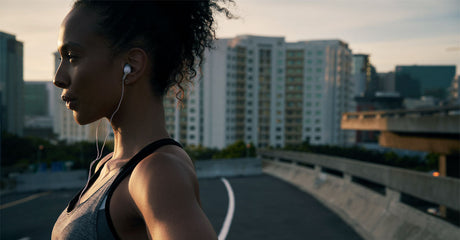 A woman wearing earbuds during a morning run on a city street.
