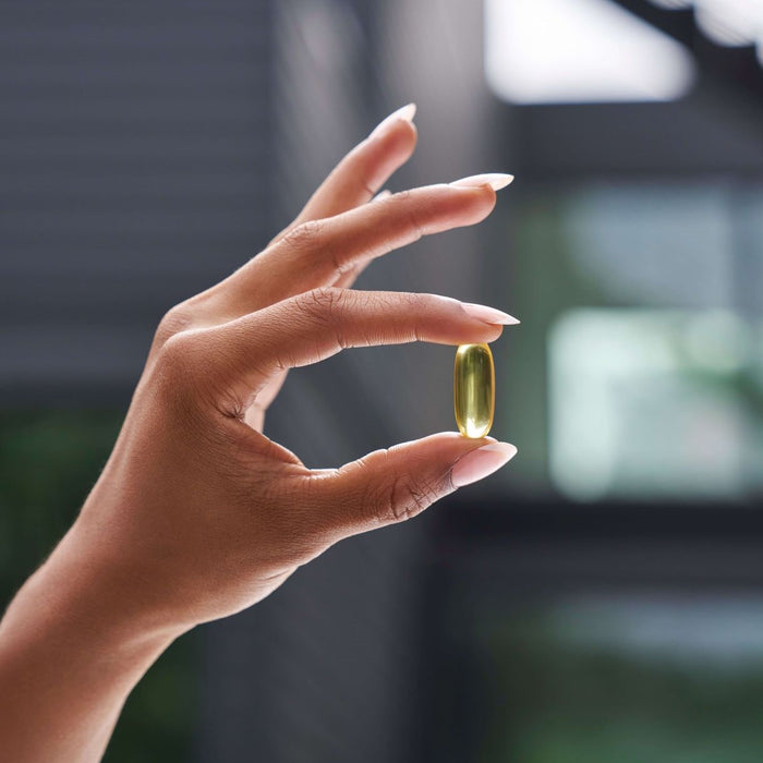 Hand holding a yellow supplement capsule against a blurred background